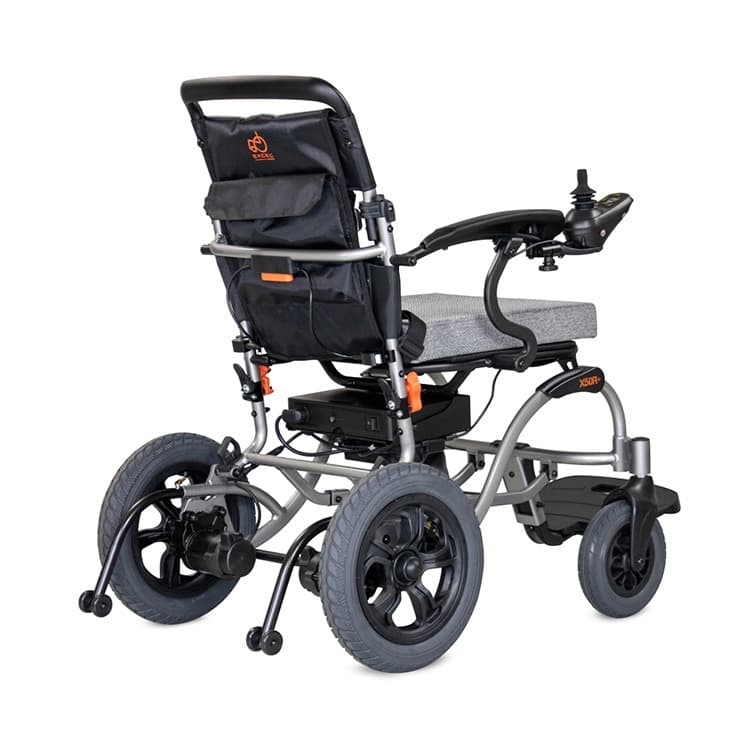 Excel X50R+ elektrische rolstoel met brede centrale voetsteun, heupgordel en joystick bediening en zwart en zilver frame met lichtgrijze bekleding en stevige rugleuning achteraanzicht tas op rugleuning en anti-kiep wieltjes