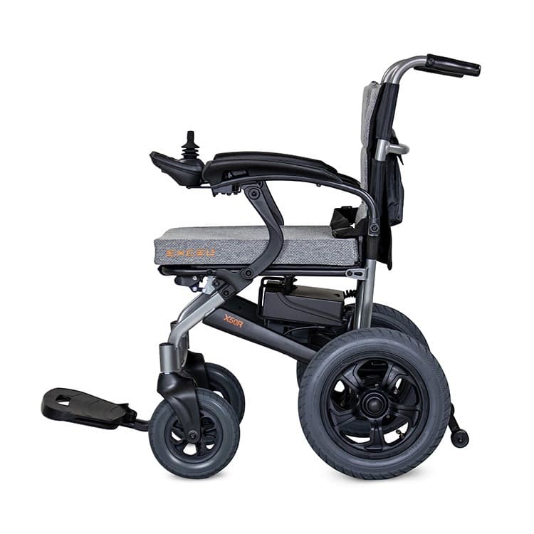 Excel X50R elektrische rolstoel met brede centrale voetsteun, heupgordel en joystick bediening en zwart en zilver frame met lichtgrijze bekleding zijkant met oranje logo en beletterling van excel op het zitkussen en zijframe