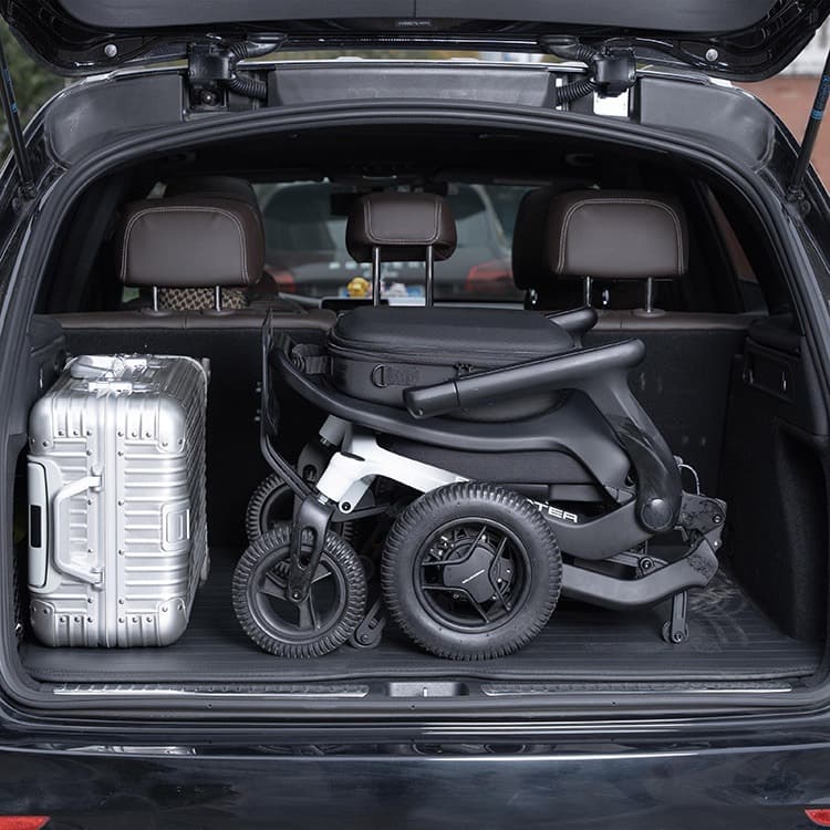 Revamed Robooter E80 Elektrische rolstoel zwarte bekleding en frame met verloop naar wit vooraan het frame. Voetensteun in het midden van de rolstoel en bestuuringsjoystick aan het uiteinde van de armleuning. Sfeerbeeld opgeklapt in de kofferbak van een a