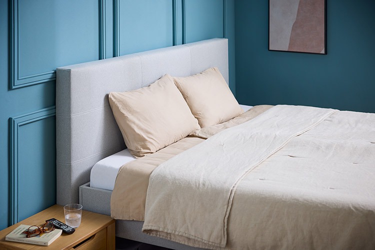 Deron Timeless Deluxe tweepersoons hoog-laagbed lichtgrijs verstelbare lattenbodem sfeerbeeld opgemaakt bed met hoofdbord (niet standaard inbegrepen) met beige linnen, blauwe muur, houten nachtkastje met spulletjes erop